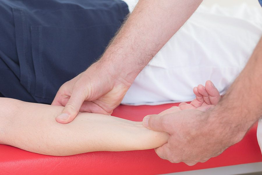 Heilmasseur behandelt den Unterarm eines Patienten auf einer roten Therapieliege